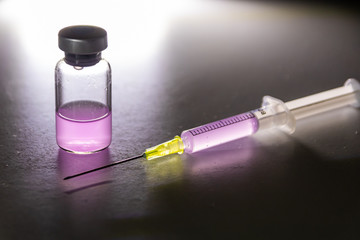 Leuchtende Spritze mit pinkfarbenem Heilmittel aus einer medizinischen Ampulle zur Therapie von...