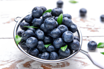 Sieve with ripe blueberry on light wooden background