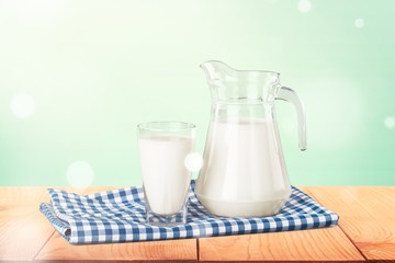 A glass of milk and a milk jug on plaid tablecloth