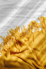 Bedding with a yellow knitted plaid. Cozy background with copy space. Hygge concept.