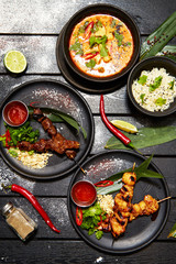 Asian dishes on a black table. Satay and Tom Yam
