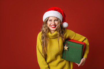 Beautiful young woman with Christmas gift on color background