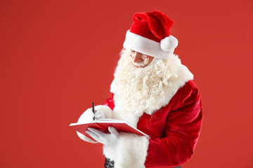 Portrait of Santa Claus with notebook on color background