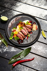 Asian dish on a black plate. Duck breast with peach