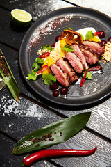 Asian dish on a black plate. Duck breast with peach
