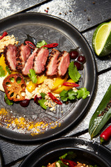 Asian dish on a black plate. Duck breast with peach