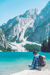 Fototapeta premium man sitting on the beach of the lake with backpack mountains in background