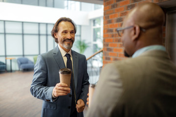 Businessman drinking coffee while waiting for elevator with colleague