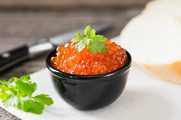 Red caviar in black bowl on wooden background