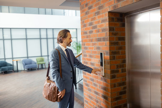 Businessman with brown leather bag calling for elevator