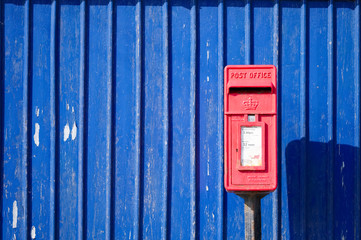 Red Royal Mail post box against blue background wall still in use