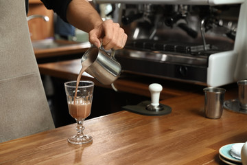 Fototapeta na wymiar Barista pouring coffee into glass at bar counter, closeup. Space for text