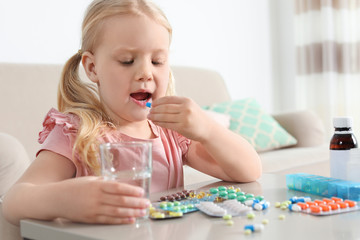 Little child taking pill at table indoors. Danger of medicament intoxication