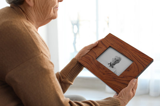 Elderly woman with framed photo of her son at home