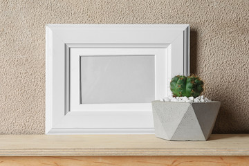 Blank frame and succulent plant on wooden table near brown wall, space for design. Home decor