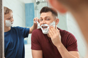 Son applying shaving foam on dad's face at mirror in bathroom
