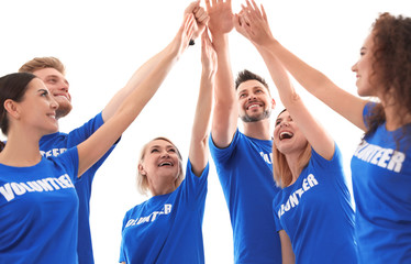 Team of volunteers putting hands together on light background