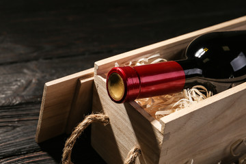 Crate with bottle of wine on wooden table, closeup