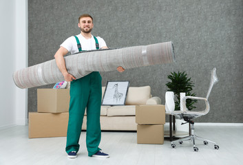 Young worker carrying rolled carpet in room. Moving service