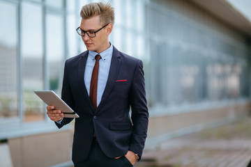 Elegant young businessman using his PC tablet. Portrait of a Male executive manager in trendy clothes with tablet pc in front of office building. Modern technology concept