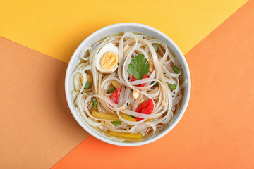 Tasty ramen with rice noodles and vegetables on color background, top view
