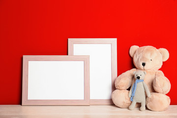 Soft toys and photo frames on table against red background, space for text. Child room interior