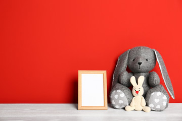 Soft toys and photo frame on table against red background, space for text. Child room interior
