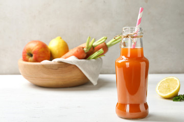 Fototapeta na wymiar Bottle of fresh carrot juice and ingredients on white wooden table against light background, space for text