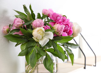 Shelf with vase of beautiful peonies on white wall