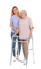 Caretaker helping elderly woman with walking frame on white background