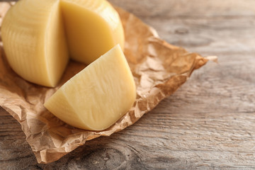 Parchment paper with cut wheel of delicious cheese on wooden table. Space for text