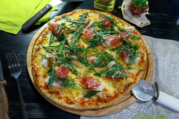 Pizza with bacon, cheese and herbs on a wooden dish on a black wooden background
