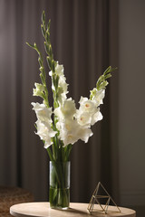 Vase with beautiful white gladiolus flowers on wooden table in room