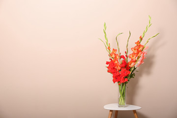 Vase with beautiful gladiolus flowers on wooden table against beige background. Space for text