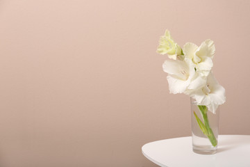 Vase with beautiful gladiolus flowers on wooden table against beige background. Space for text