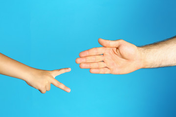 Little child and his father playing rock, paper and scissors on blue background, closeup