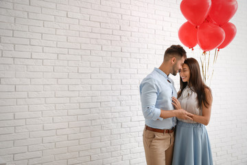 Obraz na płótnie Canvas Young couple with air balloons near white brick wall. Celebration of Saint Valentine's Day