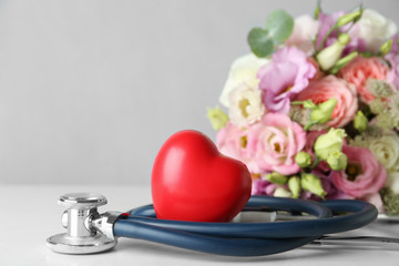 Red heart, stethoscope and bouquet on white table. World health day