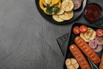 Delicious grilled sausages and vegetables on grey table, flat lay. Space for text