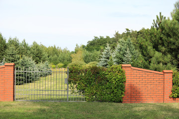 Ogrodzenia, metalowa brama i mur z cegły czerwonej.