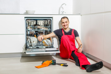 Young Male Technician Checking Dishwasher With Digital Multimeter In Kitchen
