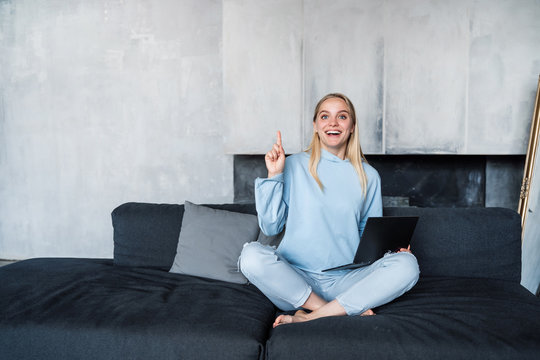 Image of happy woman using silver laptop while sitting on sofa
