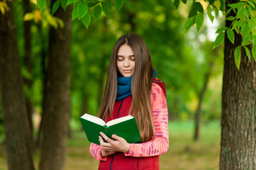 Fototapeta premium Young romantic girl reading a book sitting on the grass