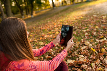 Fototapeta na wymiar young girl taking picture digital tablet pc in autumn park