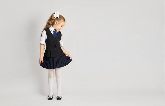 The little girl tried on a school uniform for the first time. A girl in a school  uniform looks at herself from the side. Little girl in uniform on a white  background.