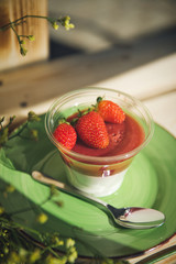 Panacota with strawberries in a cup on a wooden background with flowers