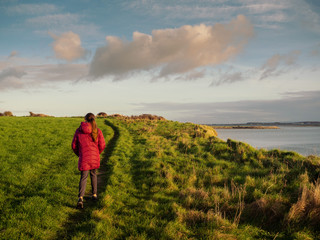 Girl walking on a path in a field by the ocean, Outdoor activity by teenager. Cloudy blue sky.