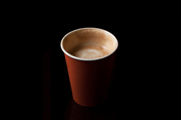 Half drunk latte coffee in an orange disposable paper cup isolated on black. Centered.