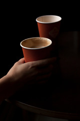 Woman holding a disposable orange cup with latte. Low key dark shot.