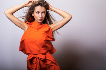 Young model woman in orange dress pose in studio.